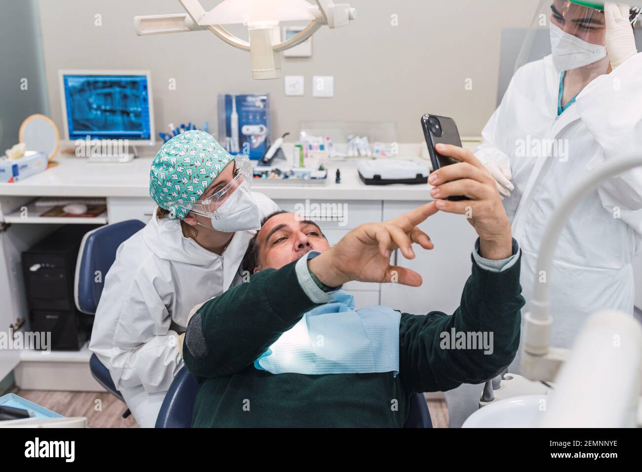 Paziente che prende un selfie nello studio dentistico. Tre persone. Medico femminile. Concetto di accoglienza e benessere. Sorrisi Foto Stock