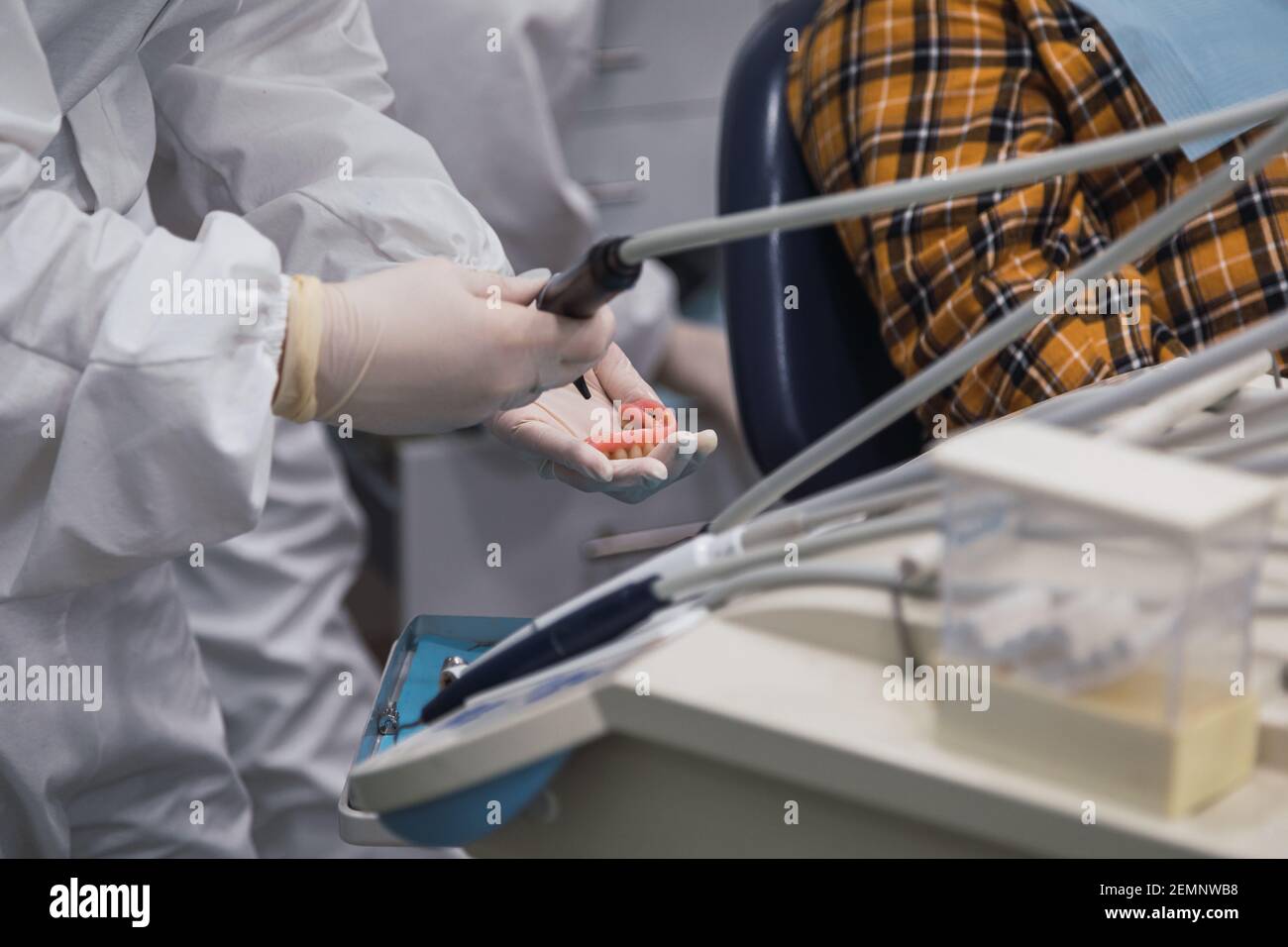 Mani di un tecnico dentale con maschera chirurgica e vetri che lucidano le protesi sulla sua tabella. Concetto di salute Foto Stock