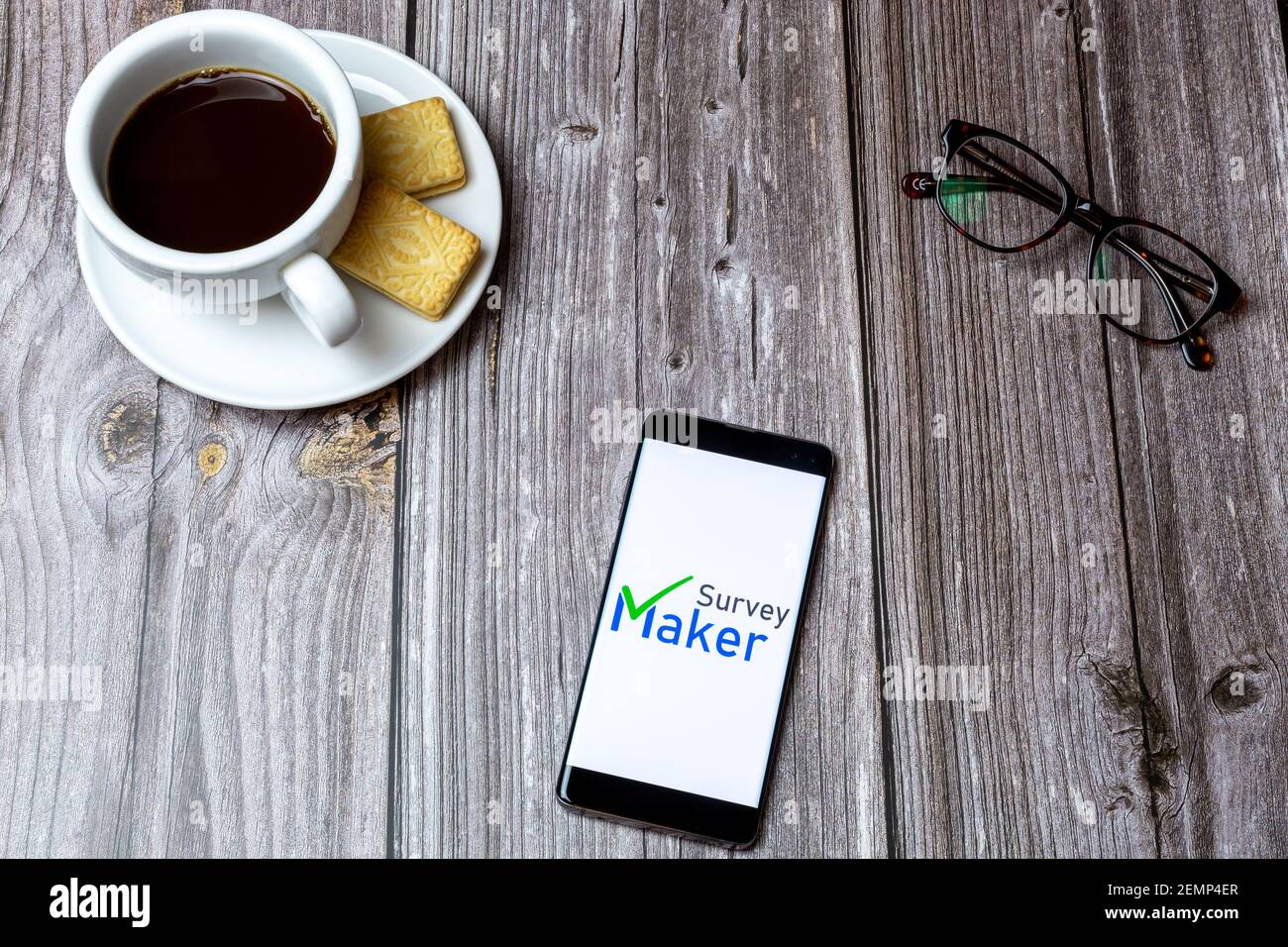 Un telefono cellulare o cellulare su un tavolo di legno Con l'app Survey Maker aperta accanto a un caffè e bicchieri Foto Stock