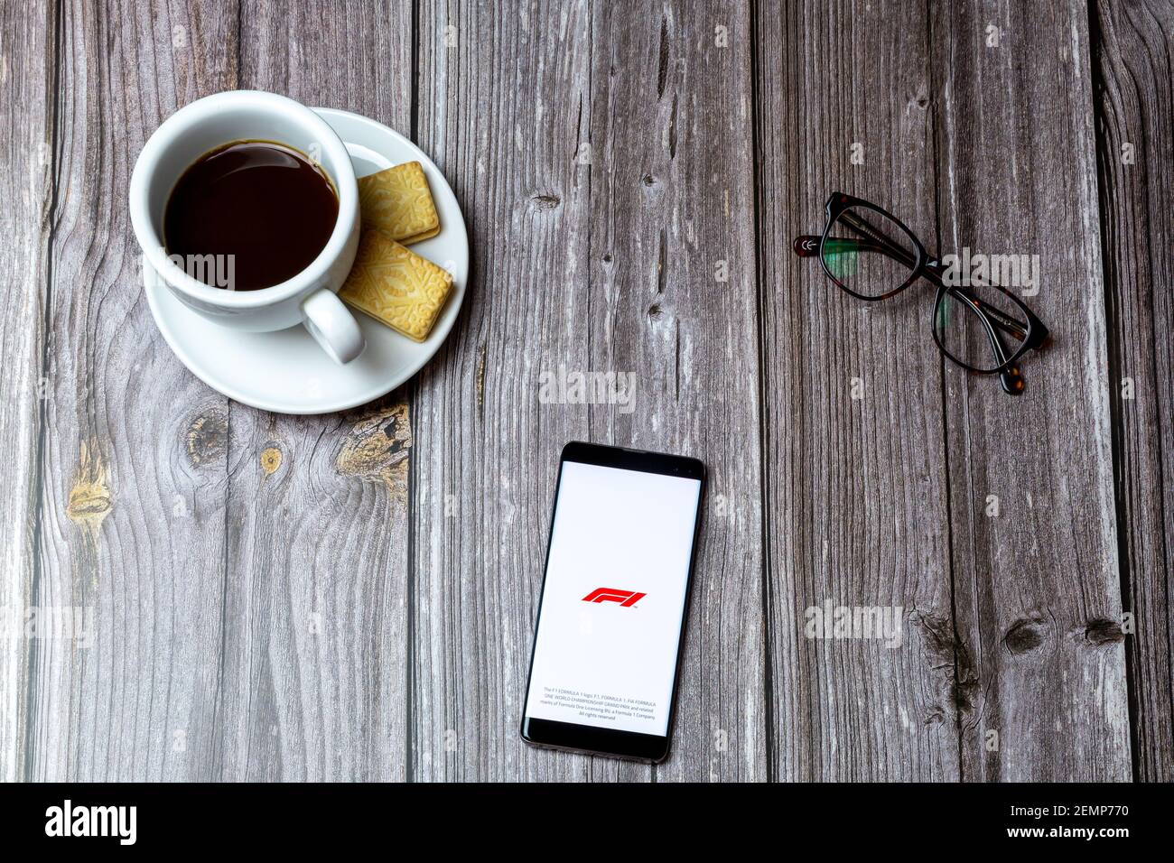 Un telefono cellulare o cellulare su un tavolo di legno Con l'app F1 aperta accanto a un caffè e. occhiali Foto Stock