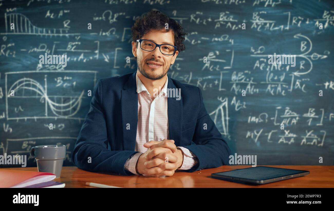E-Education online: Insegnante seduto alla scrivania, spiega lezione a una classe, dietro di lui Blackboard con scrittura. E-Learning, Corsi online: Docente Foto Stock