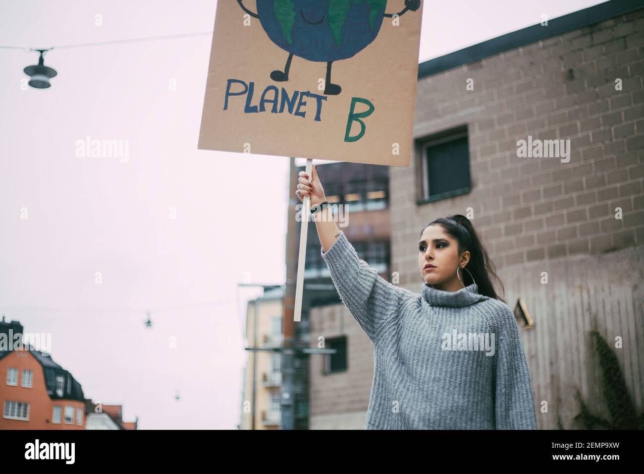 Attivista femminile che guarda via mentre tiene il manifesto della terra del pianeta durante movimento sociale Foto Stock