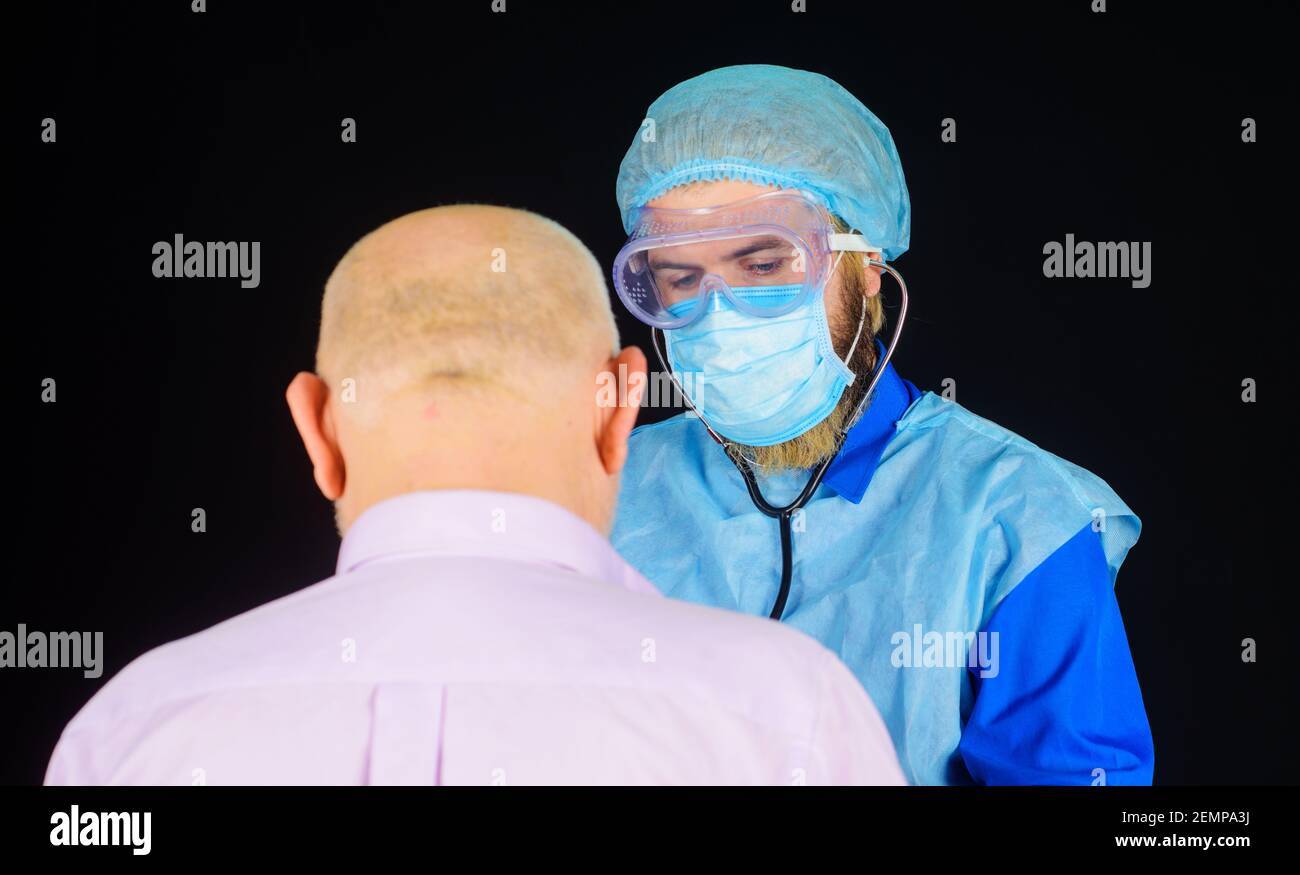 Medico in maschera con stetoscopio che controlla il paziente. Uomo malato in ospedale. Covid-19. Coronavirus. Concetto di assistenza sanitaria. Foto Stock