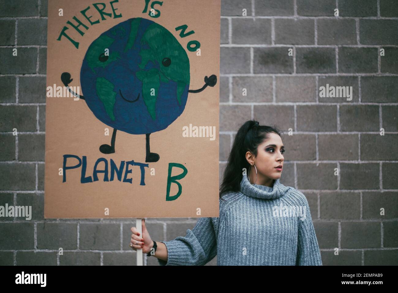Attivista femminile che guarda via mentre tiene il manifesto della terra del pianeta contro parete Foto Stock