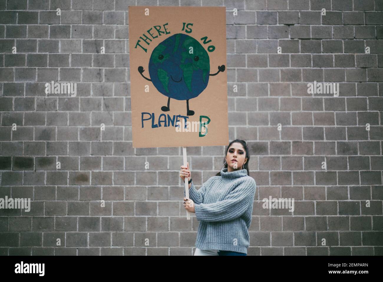 Giovane attivista femminile che tiene il pianeta terra poster contro muro durante movimento sociale Foto Stock