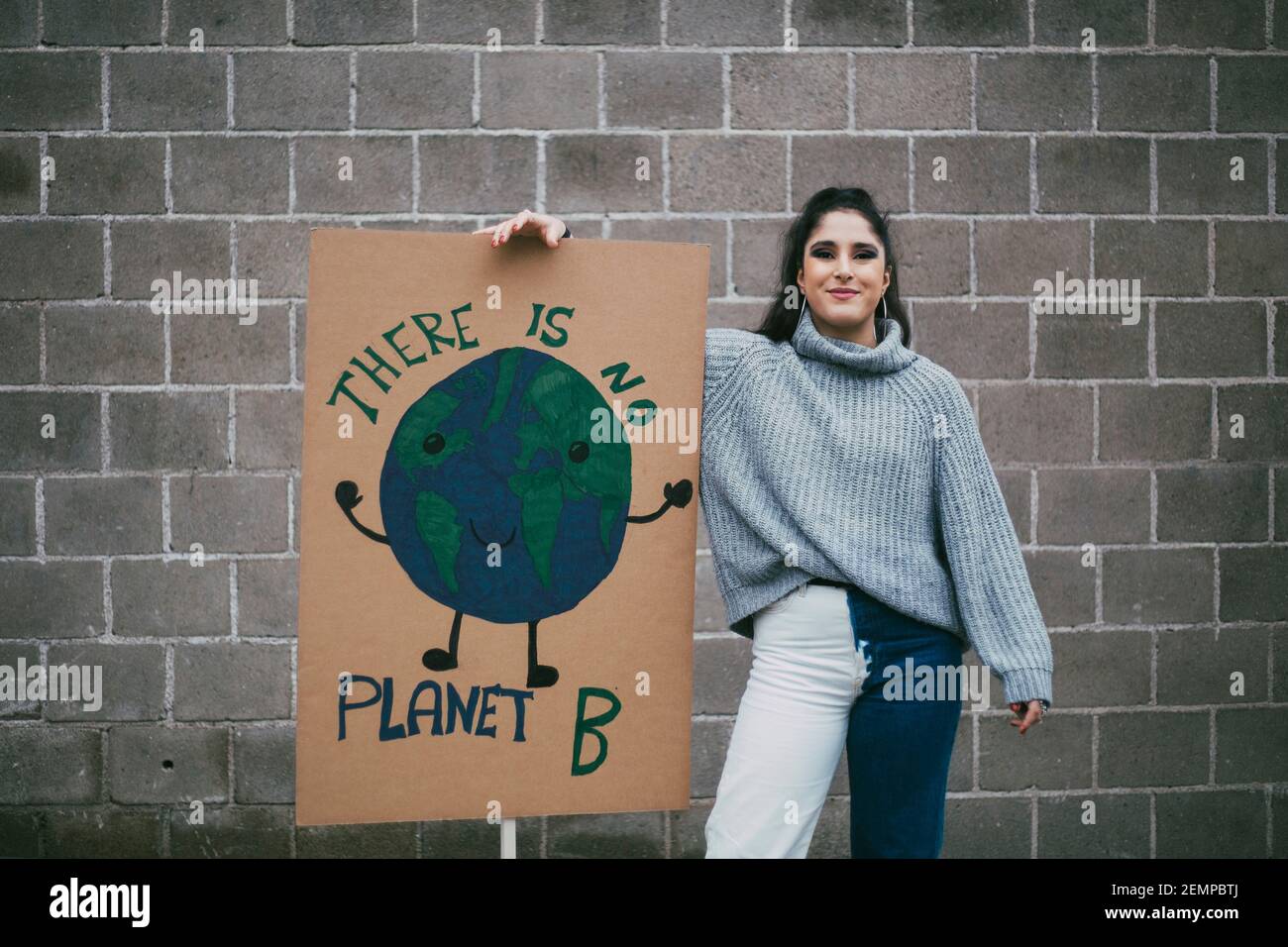 Ritratto di sorridente attivista femminile in piedi accanto al pianeta terra poster contro muro Foto Stock