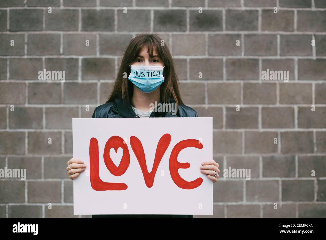 Giovane donna protestore con manifesto d'amore contro il muro durante la pandemia Foto Stock