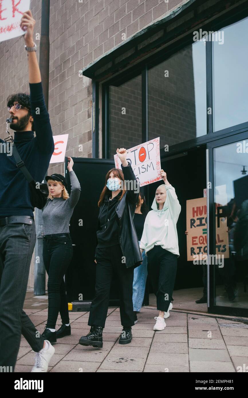 Giovane protestore maschile e femminile con stop al razzismo fuori dell'edificio durante la pandemia Foto Stock