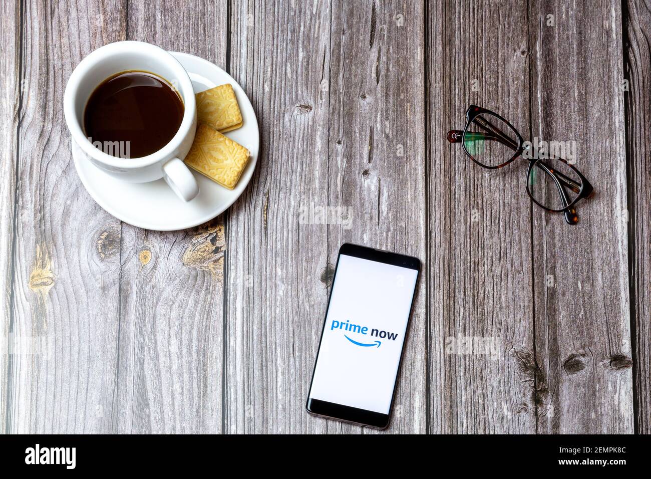 Un telefono cellulare o cellulare su un tavolo di legno Con l'app Amazon prime Now aperta accanto a caffè e bicchieri Foto Stock