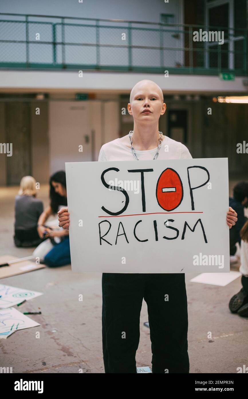 Giovane attivista femminile con poster di stop al razzismo in piedi in costruzione Foto Stock