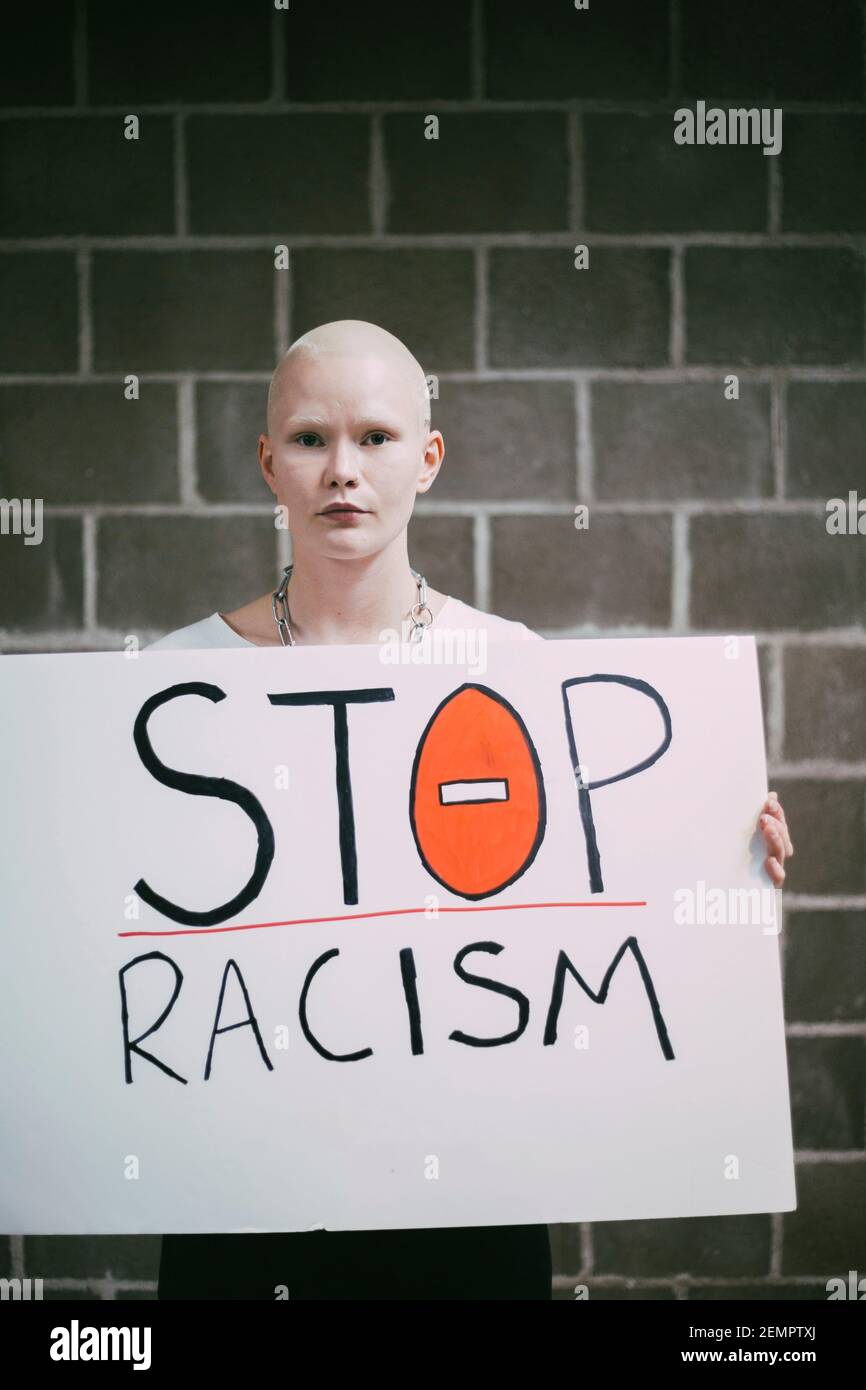 Giovane donna protestore con stop razzismo segno contro muro Foto Stock