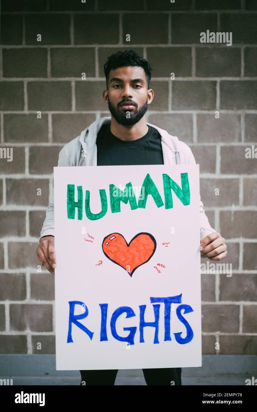 Ritratto del protestore maschile che tiene un manifesto per i diritti umani contro il muro Foto Stock