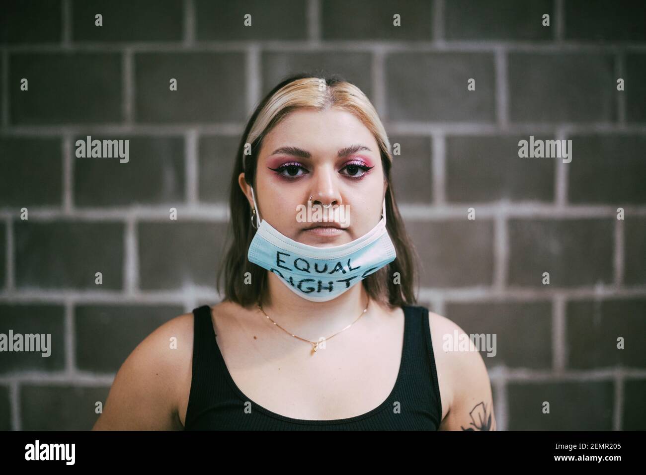 Giovane donna che indossa maschera protettiva con testo a pari diritti su di esso contro parete Foto Stock