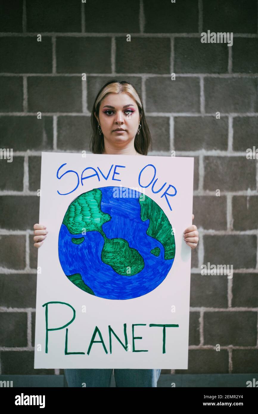 Attivista femminile con poster pianeta terra in piedi contro il muro Foto Stock