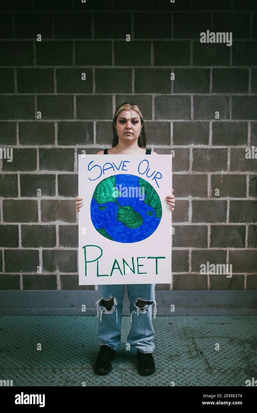 Protestore femminile con poster pianeta terra in piedi sul sentiero contro parete Foto Stock