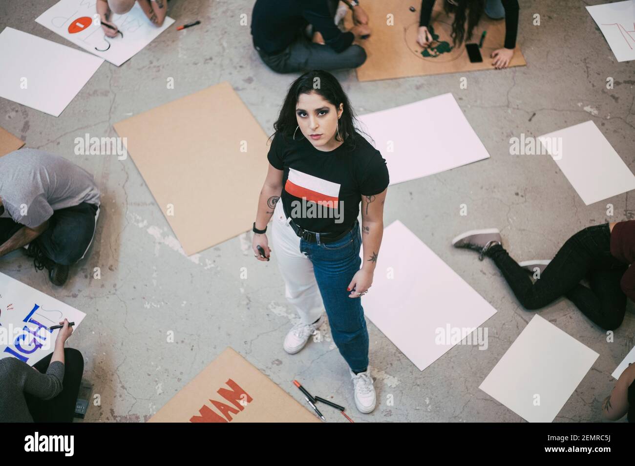 Ritratto di donna in piedi mentre si preparano attivisti maschili e femminili cartelli nell'edificio Foto Stock