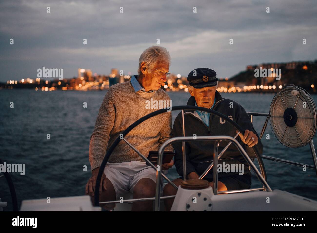 Uomo anziano che guida un amico maschio mentre navighi in barca durante il tramonto Foto Stock