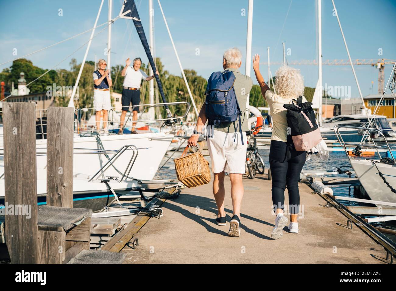 Amici anziani che sventolano alla coppia eterosessuale mentre camminano sul molo al porto Foto Stock