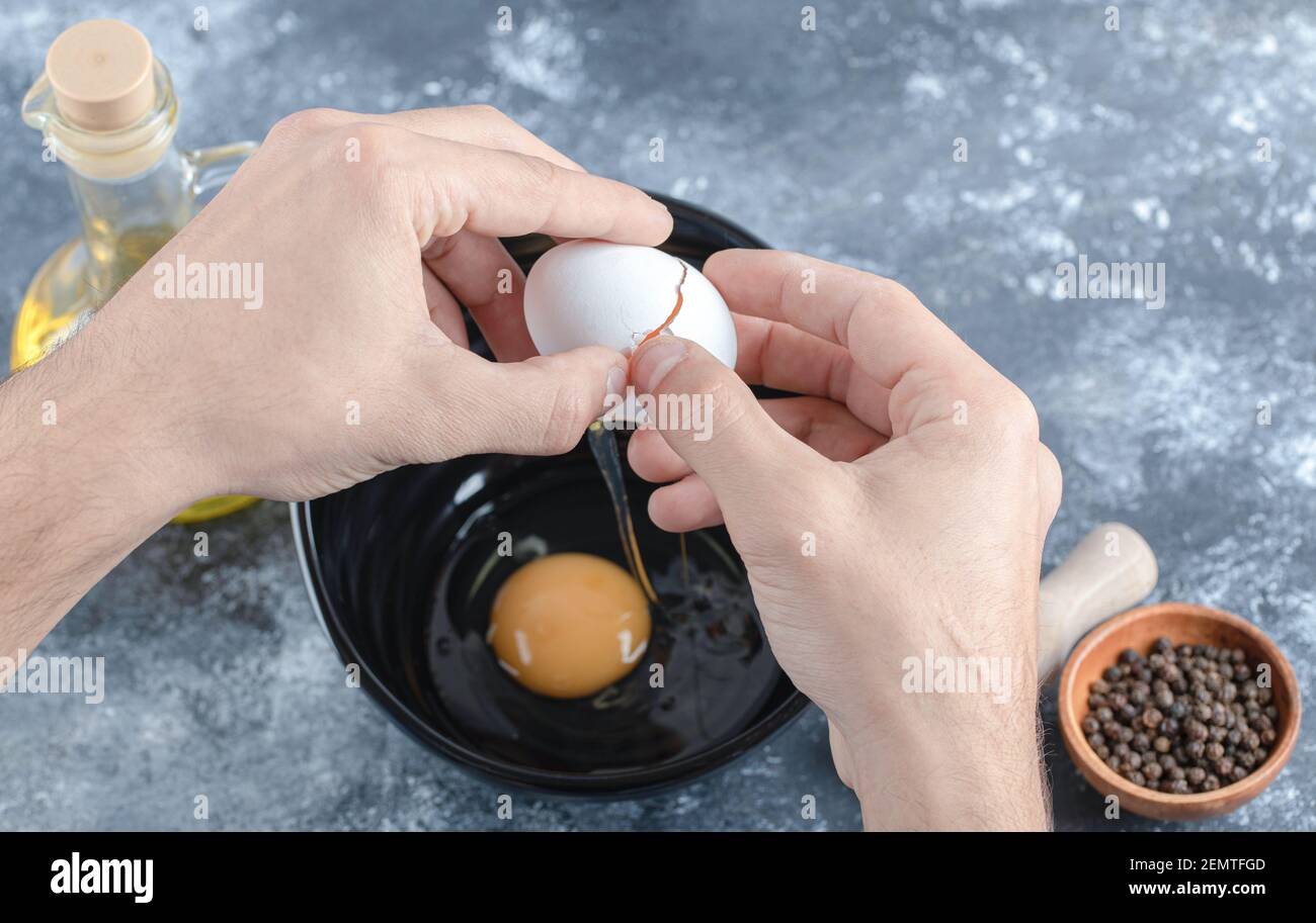 L'uomo le mani rompendo le uova in ciotola su sfondo grigio Foto Stock