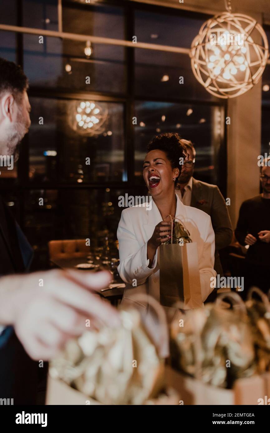 Donna d'affari allegra che ride mentre tiene la borsa del regalo al partito dell'ufficio Foto Stock