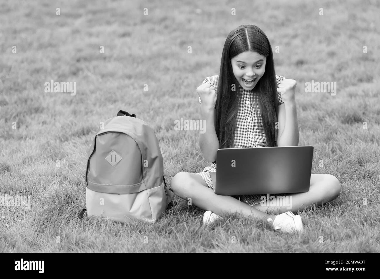 felice ragazza seduta su erba verde con il computer portatile. Start up. Bambino che gioca al computer. Torna a scuola. Formazione online. Giorno della conoscenza. Lezione privata di apprendimento dei bambini. Blogging. Foto Stock