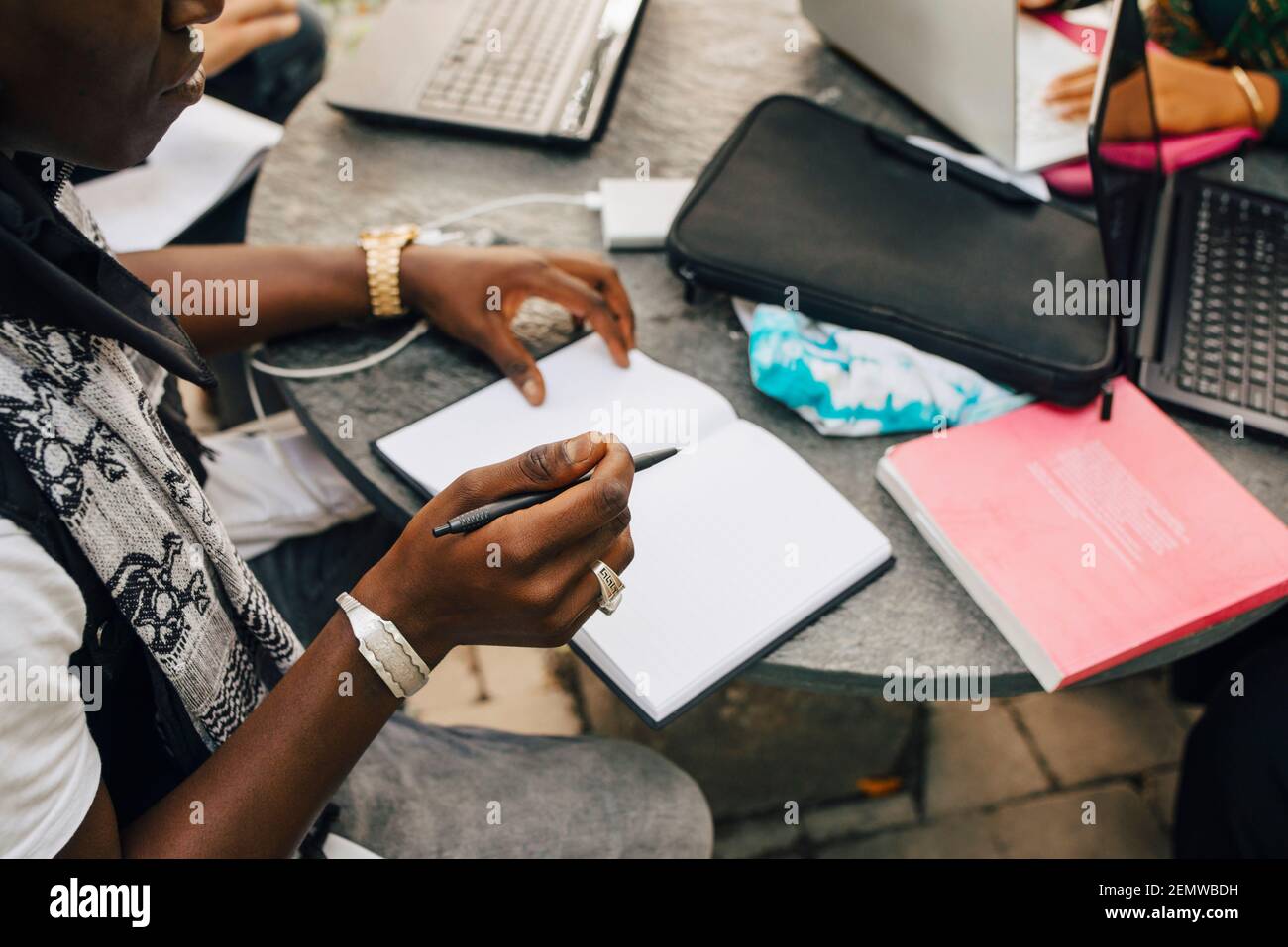 Immagine ritagliata dello studente maschile che scrive nel libro a tavola Foto Stock