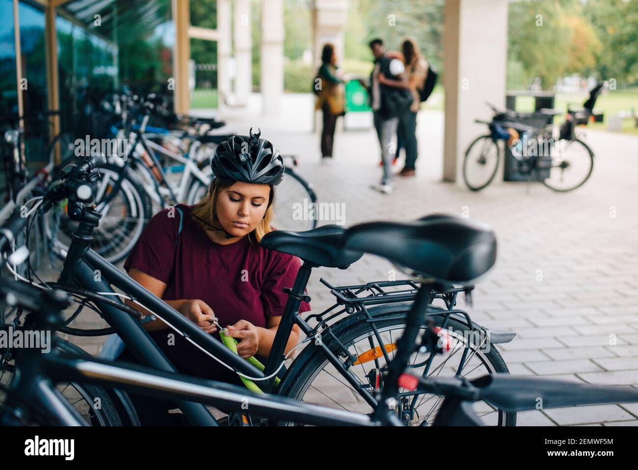 Giovane studentessa che sblocca il ciclo presso la stazione di parcheggio del campus Foto Stock