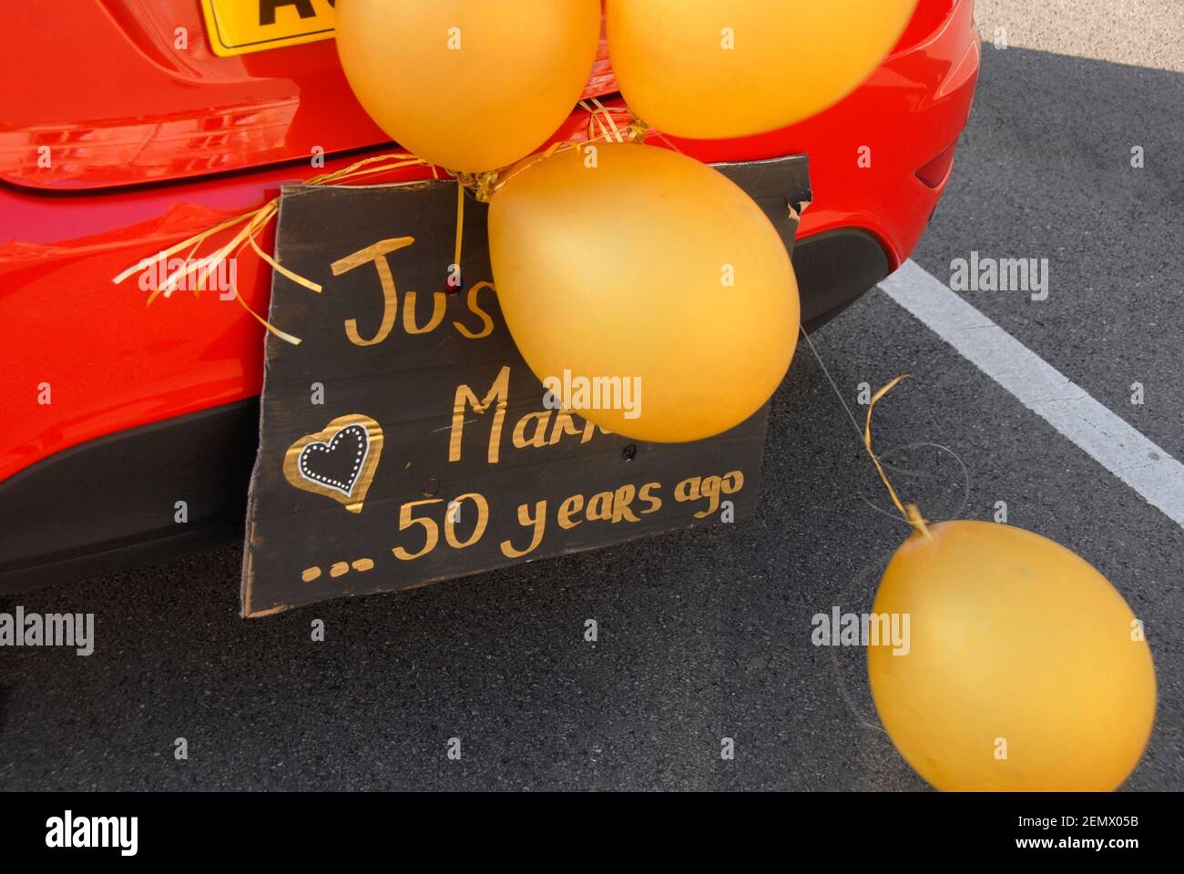 Avviso sul retro dell'auto rossa con palloncini gialli attaccati 'appena sposato. . .50 anni fa". Celebrazione del matrimonio d'oro, Inghilterra Foto Stock Avviso sul retro dell'auto rossa con palloncini gialli attaccati 'appena sposato. . .50 anni fa". Celebrazione del matrimonio d'oro, Inghilterra Foto Stock