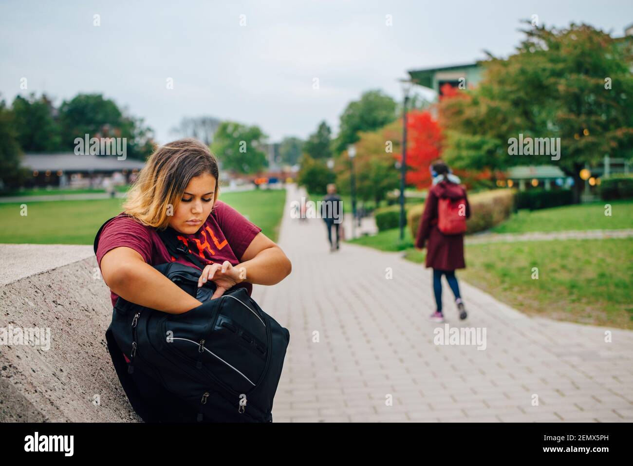 Studentessa sbirciata nello zaino mentre si trova nel campus universitario Foto Stock