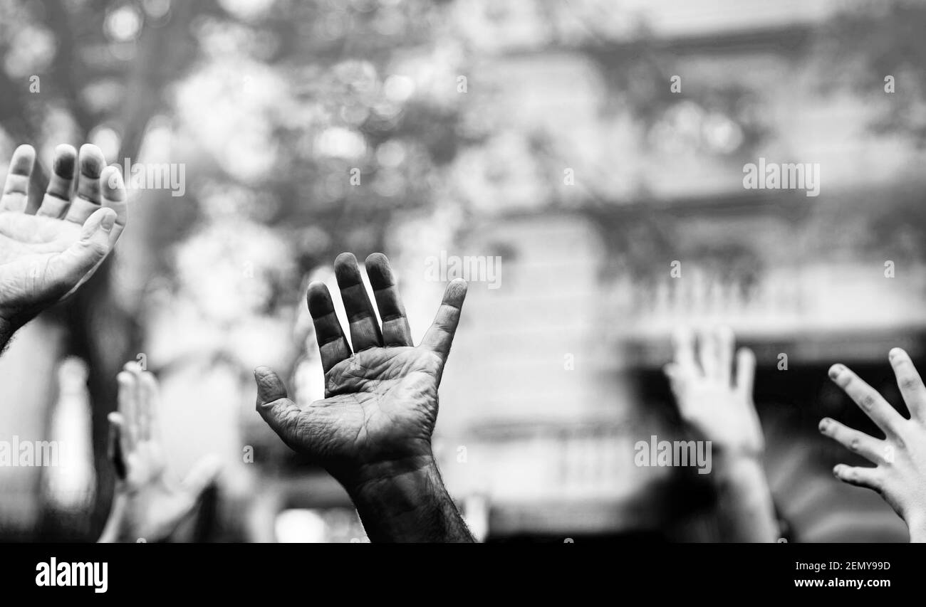 Palmo aperto di una mano nera e mani bianche sollevate nell'aria chiedendo la libertà. Mani multiculturali in una dimostrazione su strada in bianco e nero. S Foto Stock