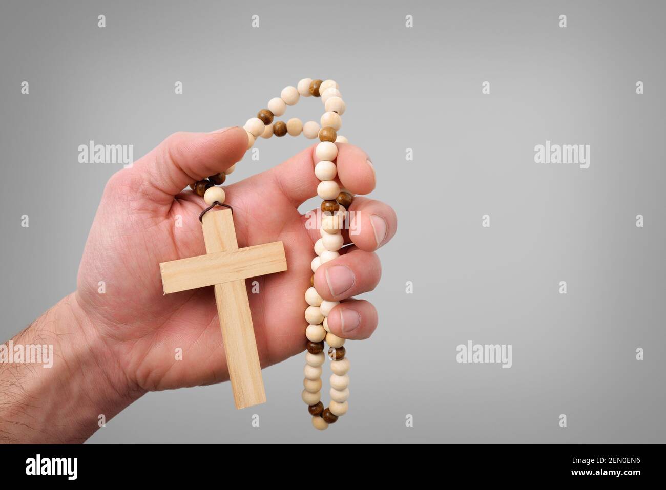 Croce cristiana di legno con perline rotonde di legno sulla mano di un credente con sfondo grigio isolato Foto Stock