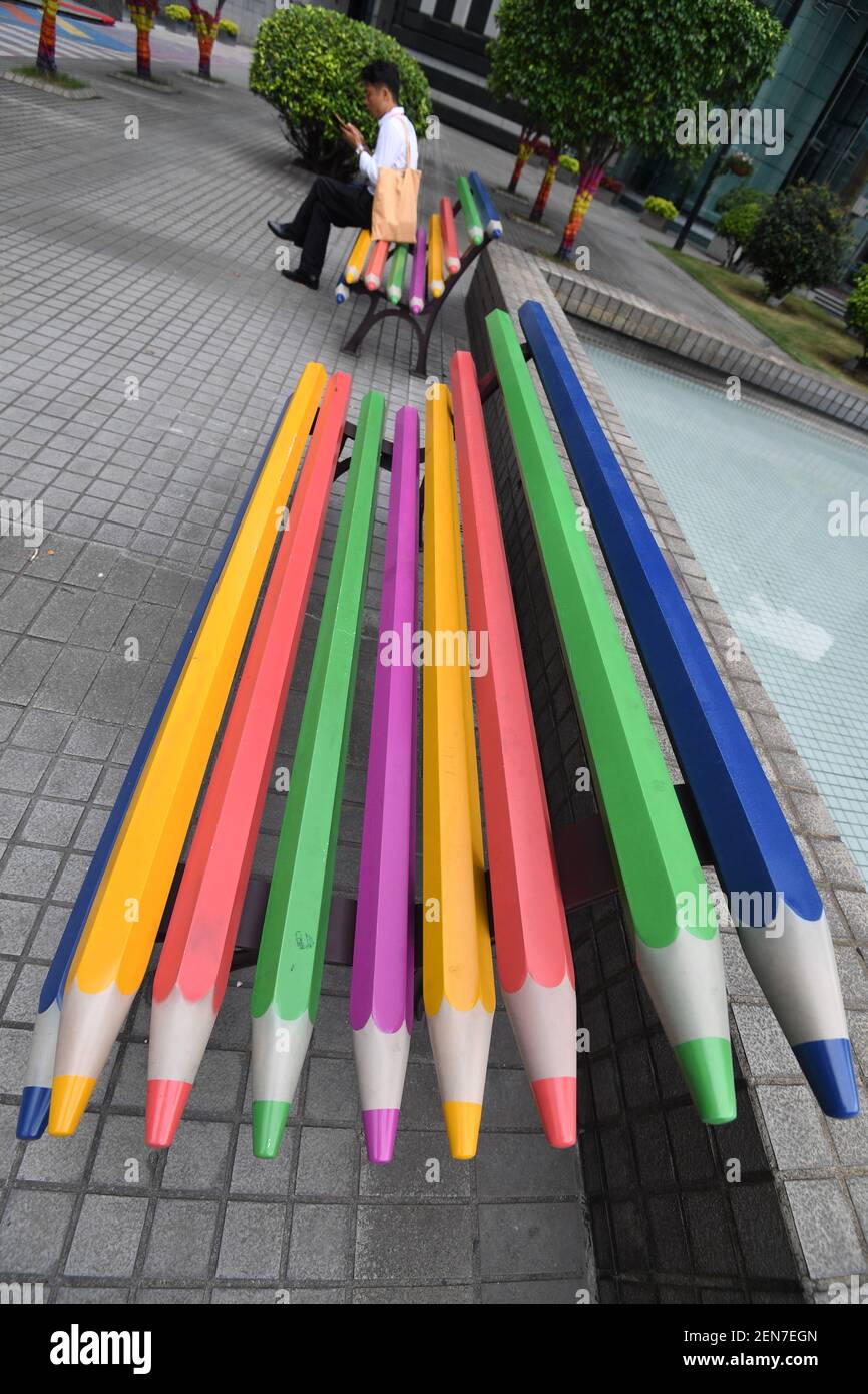 Un uomo cinese si siede su una panchina a matita colorata accanto ad altri  in una piazza tra gli edifici di uffici nella città di Guangzhou, nella  provincia di Guangdong della Cina