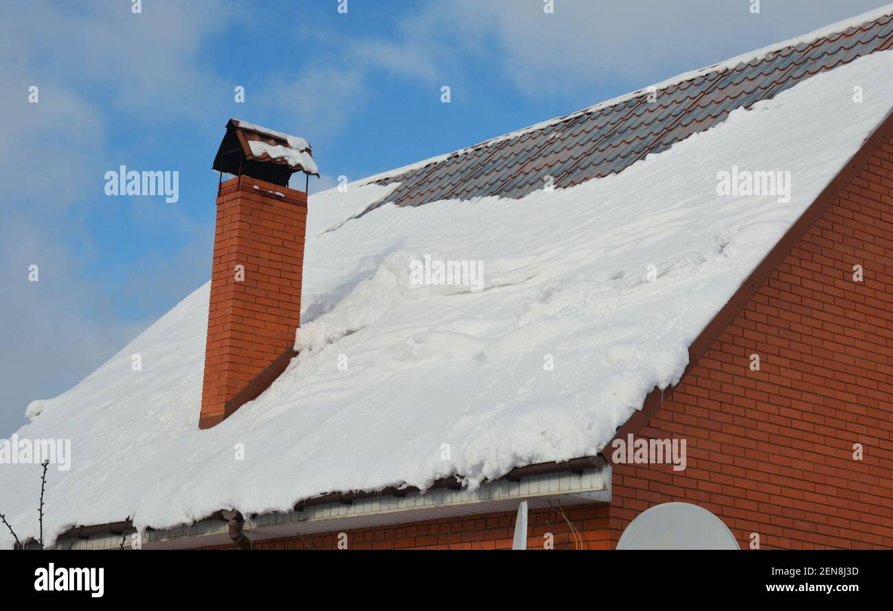 Un ripido pendio tetto in metallo coperto di neve con un camino, grondaie pioggia, ma senza guardie neve in inverno. La neve scorre, cade da un tetto in metallo. Foto Stock