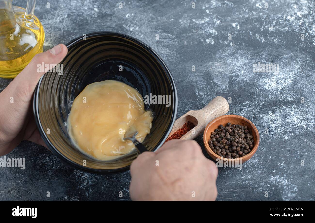 Uomo che mescola l'uovo in una ciotola nera. Su sfondo grigio Foto Stock