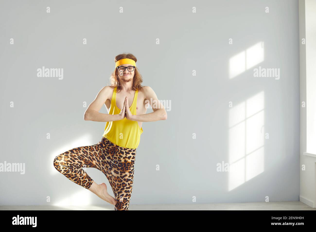 Divertente maschio con capelli lunghi e sottili in piedi in posizione meditativa praticando yoga Foto Stock