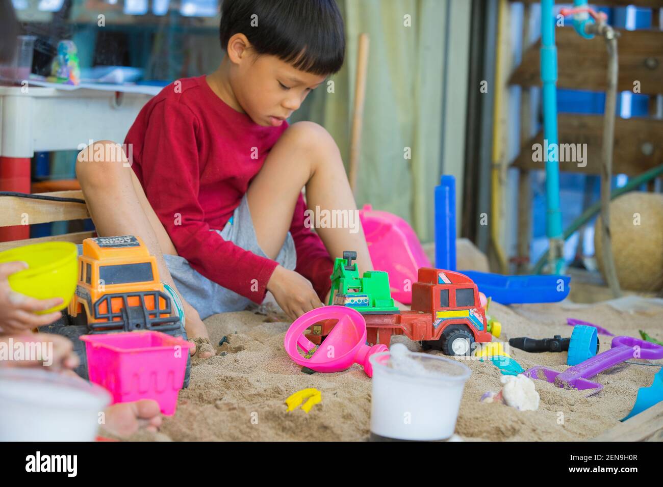Piccolo ragazzo che gioca con i bambini camion nel sandpit. Foto Stock