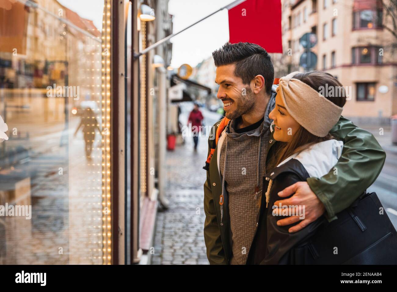 Uomo sorridente braccio intorno alla donna mentre facendo la finestra shopping dentro città Foto Stock
