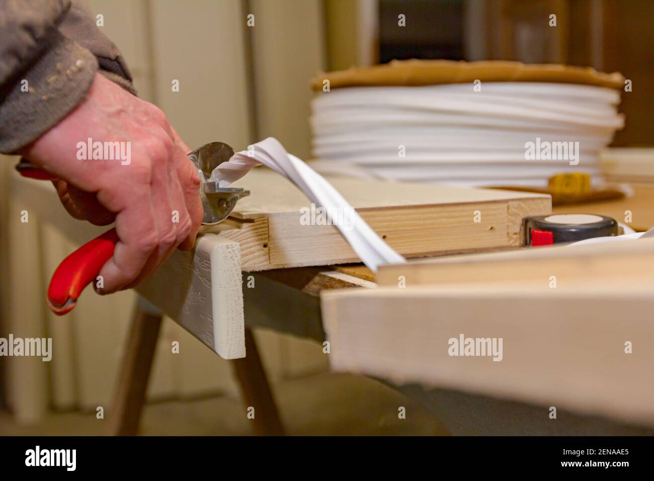 Il lavoratore di carpenteria sta tenendo le pinze metalliche rosse e il nastro di gomma di taglio che è applicato in telaio di legno della porta a carpenteria. Foto Stock