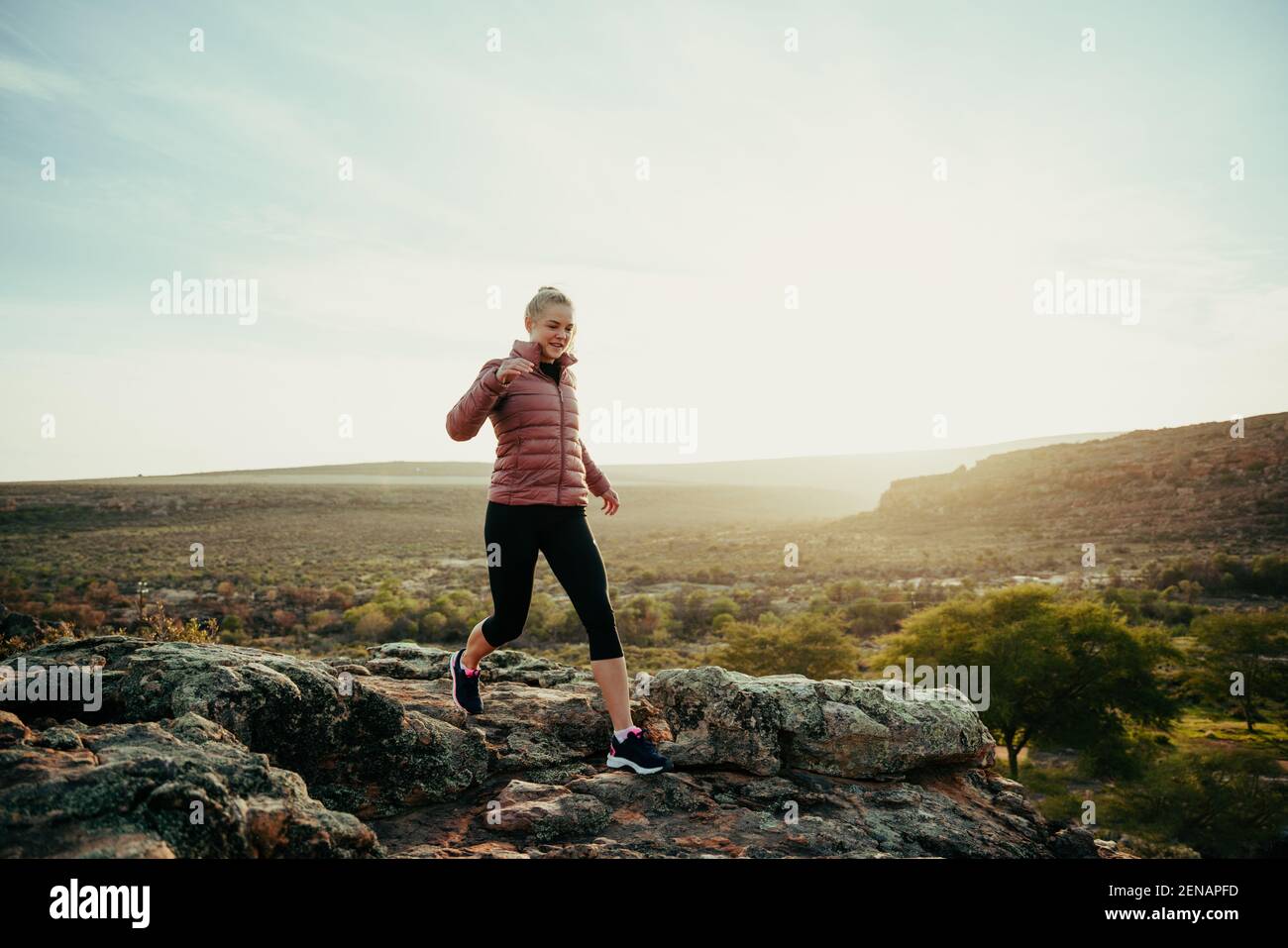 Femmina caucasica che corre in montagna lungo il sentiero escursionistico saltando giù rocce durante il tramonto Foto Stock