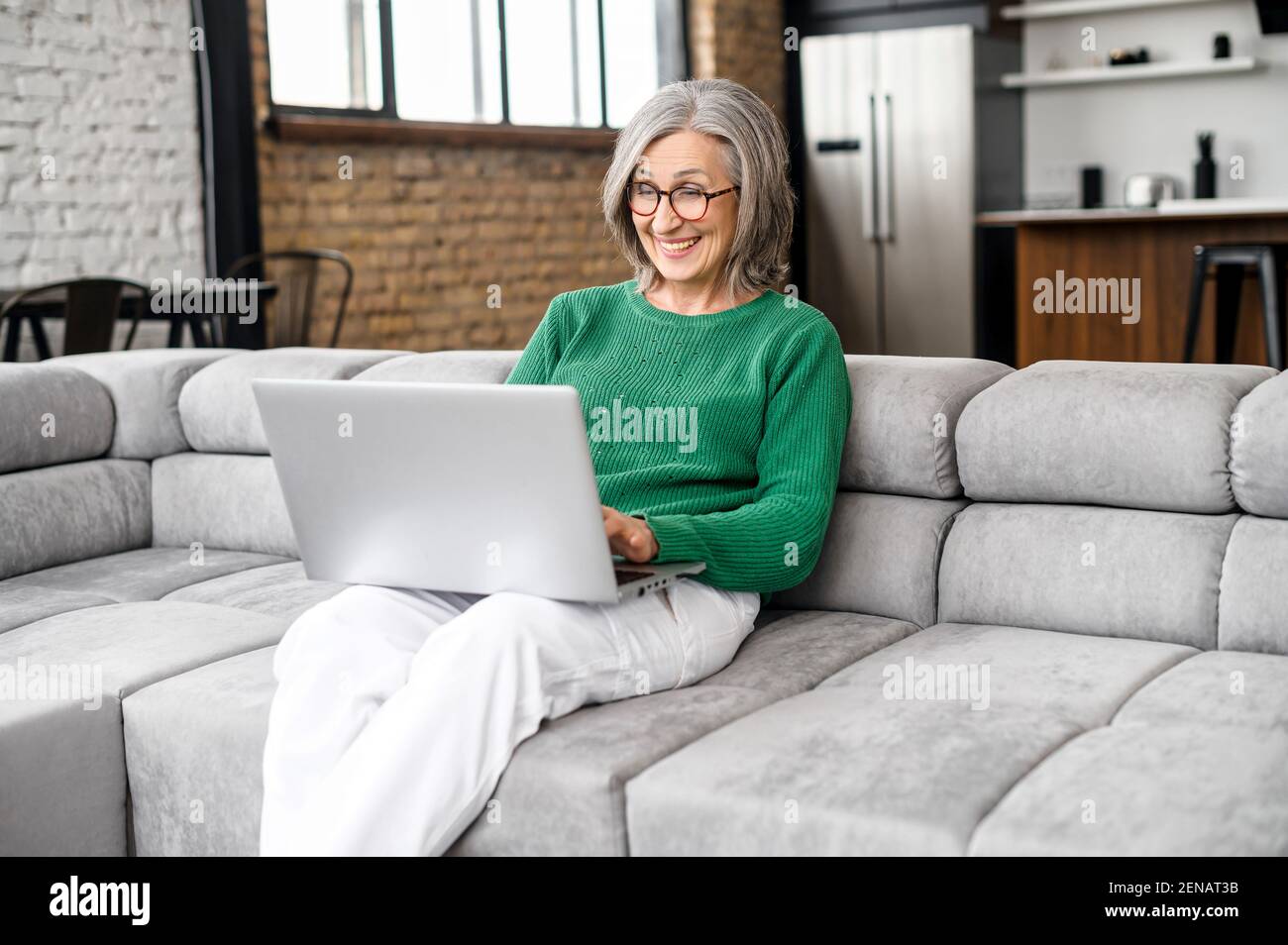 Overjoyed metà felice anni 60 donna matura in occhiali guardando lo schermo del portatile, la lettura di e-mail con le notizie stupefacenti, celebrando la vittoria della lotteria in linea, ottenendo l'approvazione del prestito della banca o il rimborso dei soldi Foto Stock