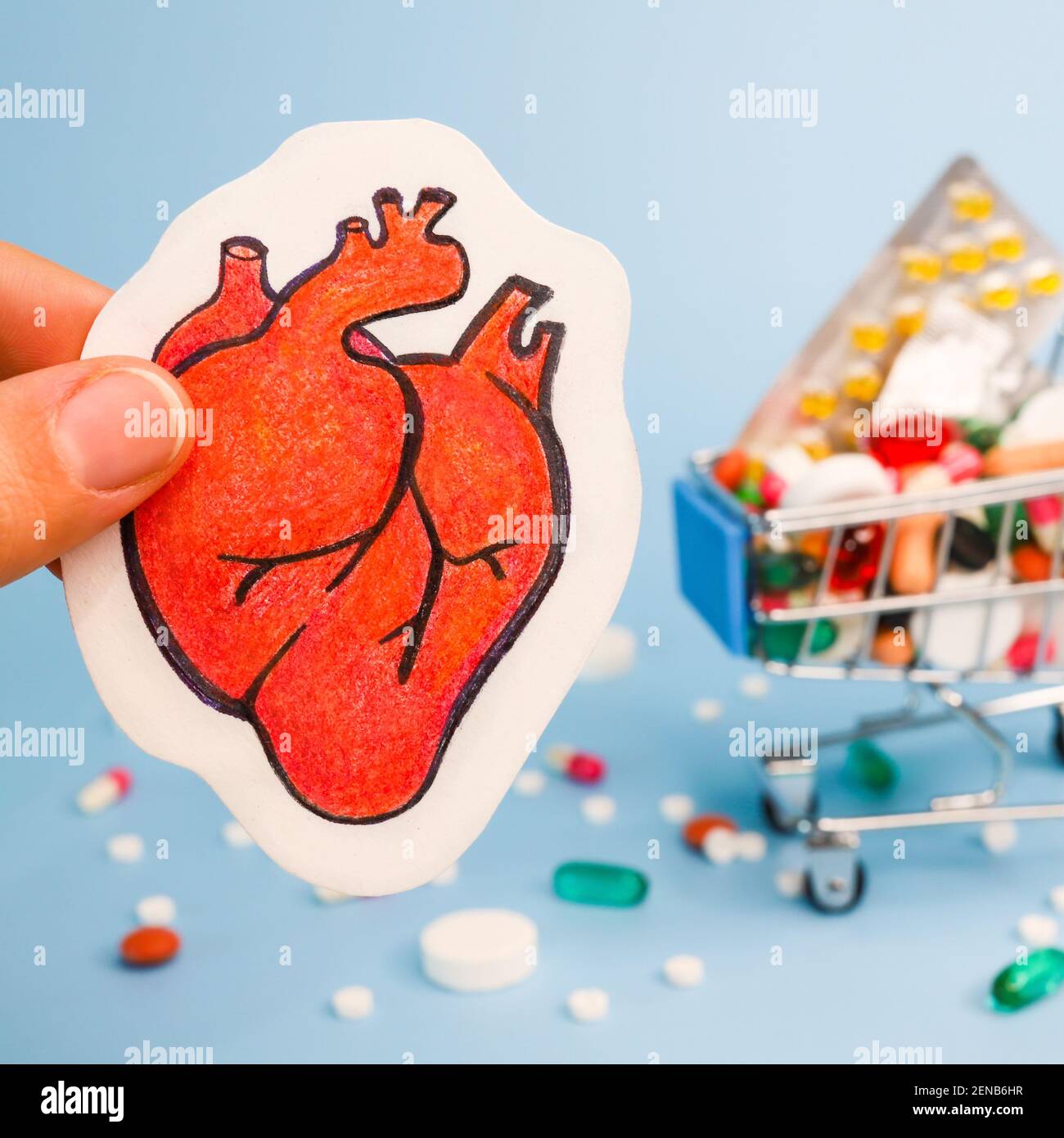 Trattamento o prevenzione di malattie cardiache con varietà di pillole. Matita disegno di cuore umano primo piano in dita sullo sfondo di molti pi colorati Foto Stock