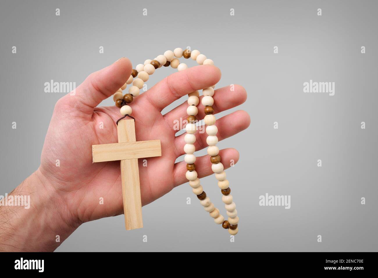 Croce cristiana di legno con perline rotonde di legno sulla mano di un credente con sfondo grigio isolato Foto Stock