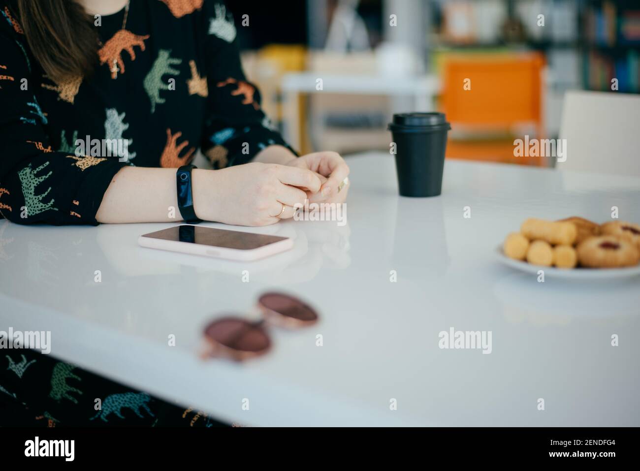 Le mani delle donne su un tavolo, una tazza nera di caffè, biscotti e occhiali da sole Foto Stock