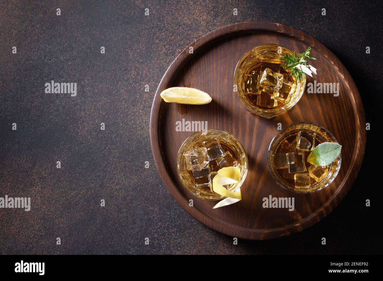 Tre bicchieri di whisky serviti sulle rocce con limone per feste su sfondo marrone. Spazio di copia. Vista dall'alto. Foto Stock