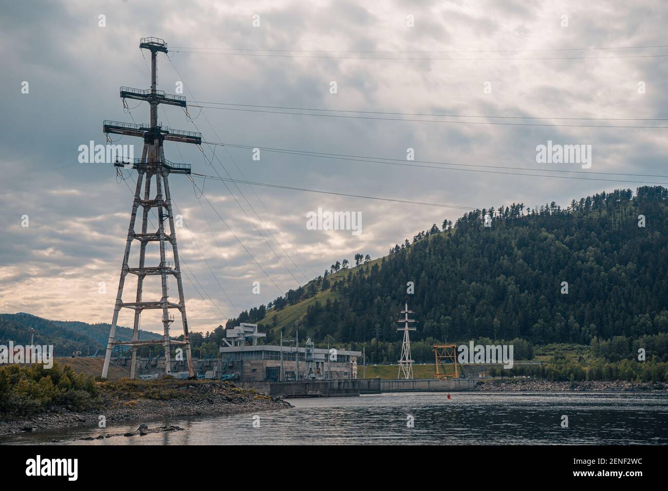 Torre elettrica ad alta tensione accanto ad una centrale idroelettrica sul fiume Yenisei. Cielo drammatico Foto Stock