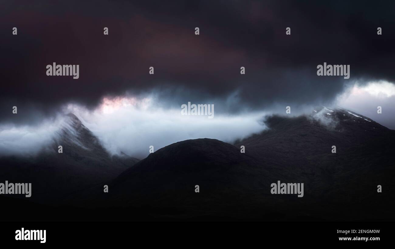 Condizioni atmosferiche estreme nelle Highlands Scozzesi all'alba. Nuvole scure sui picchi di montagna e inversione di nuvole nella valle. Foto Stock
