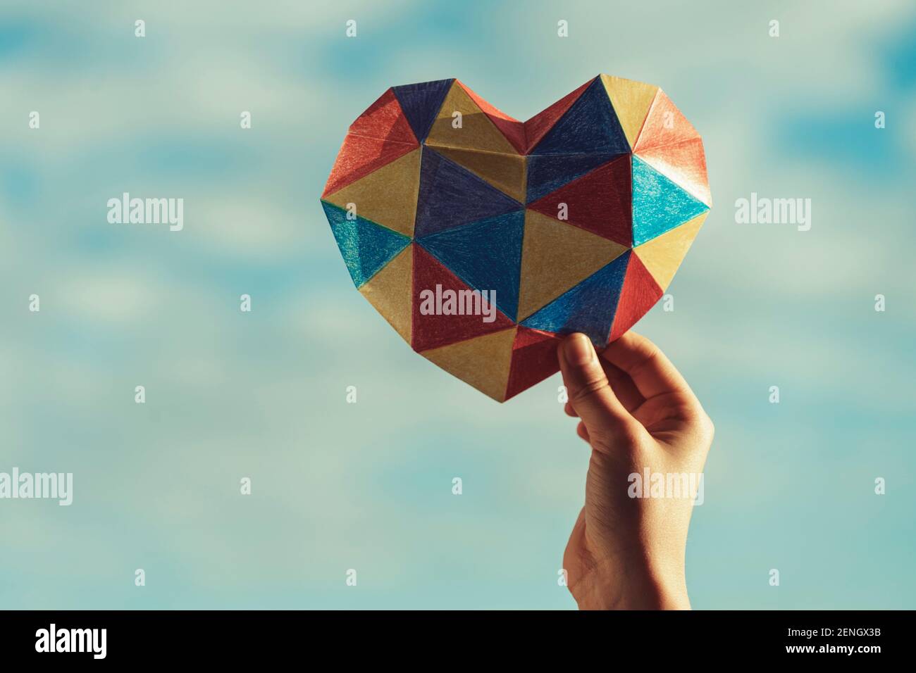Le mani del bambino tengono il cuore colorato sopra lo sfondo blu del cielo. Concetto di giorno di consapevolezza autismo mondiale Foto Stock