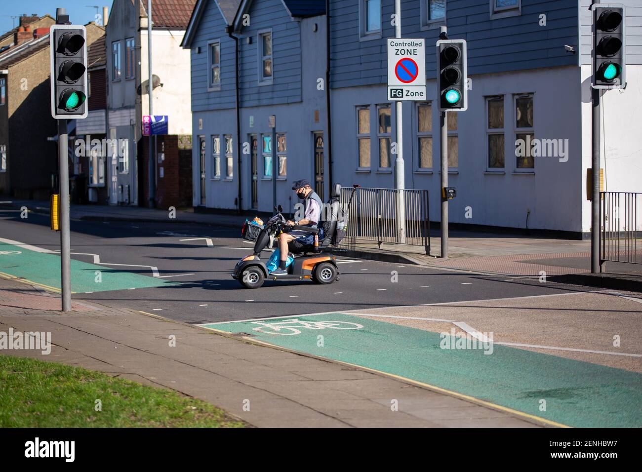 Un uomo anziano che attraversa la strada a semafori uno scooter per la mobilità Foto Stock