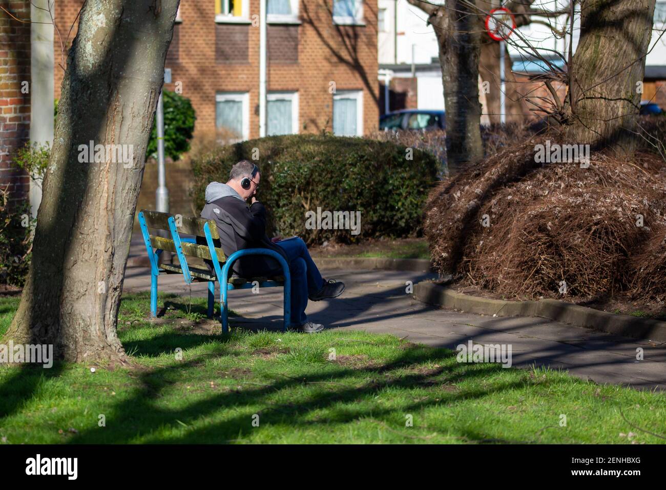 Un uomo seduto su una panchina nel parco lettura e ascoltare musica Foto Stock