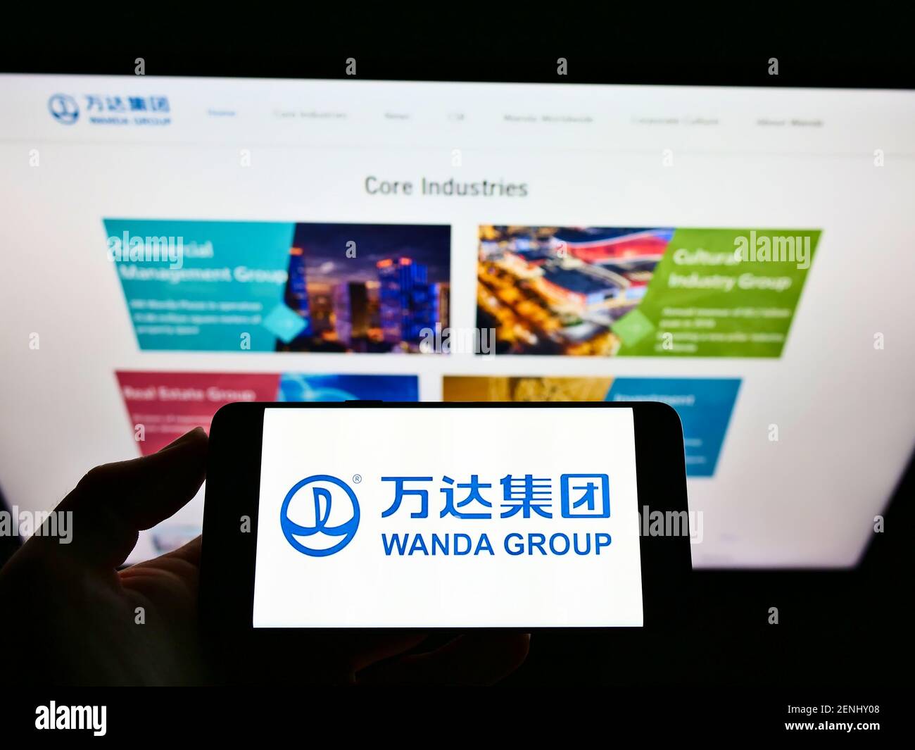 Vista ad alto angolo della persona che tiene il telefono cellulare con il logo del conglomerato cinese Wanda Group sullo schermo davanti alla pagina web. Mettere a fuoco il display del telefono. Foto Stock